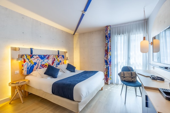 Una camera d'hotel moderna con un letto, una scrivania, una sedia e un'ampia finestra con tende.