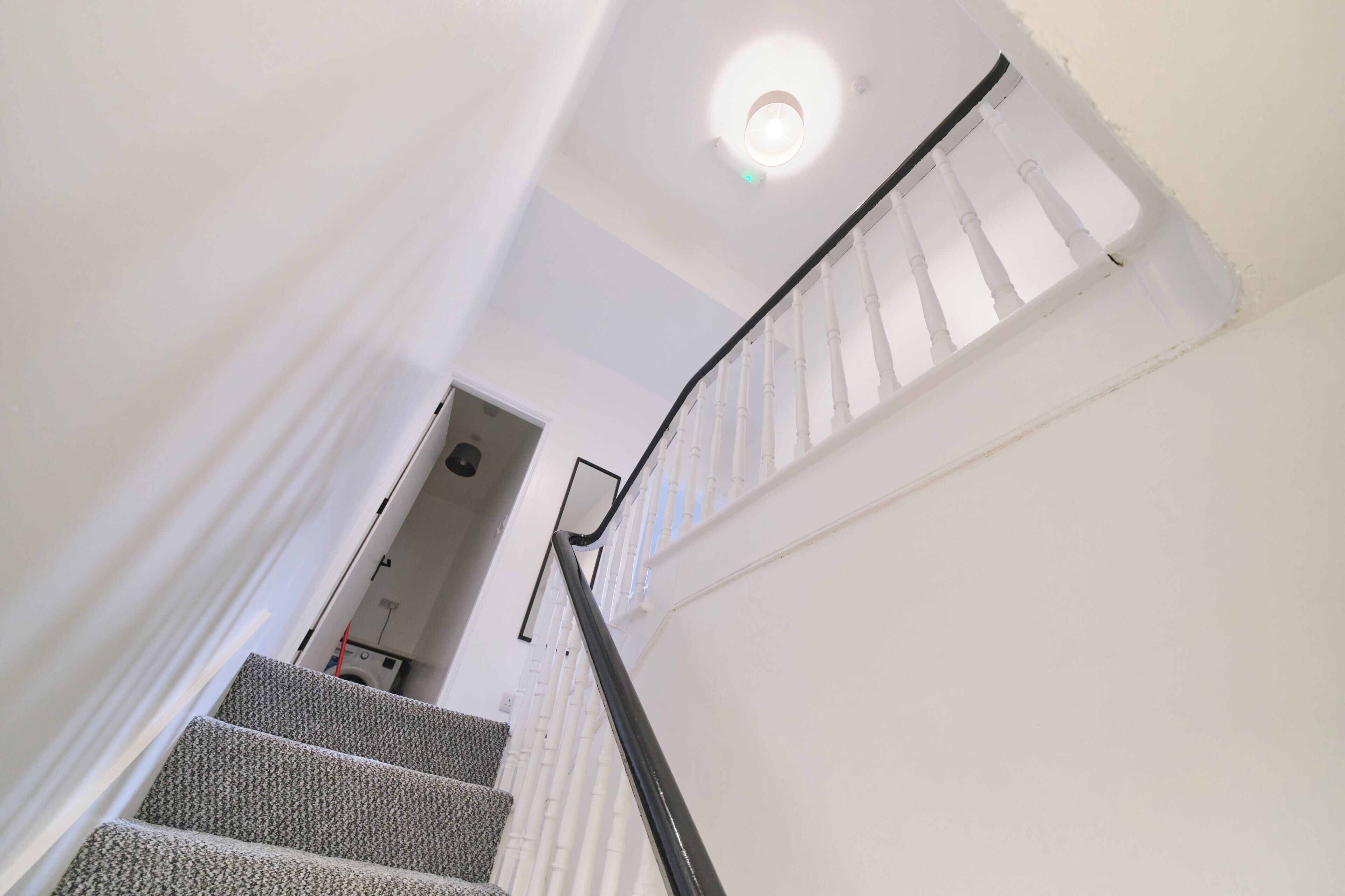 A staircase with white walls and a black handrail leading to a door.
