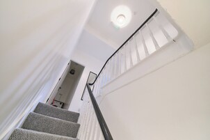 Una escalera con paredes blancas y un barandal negro que lleva a una puerta.
