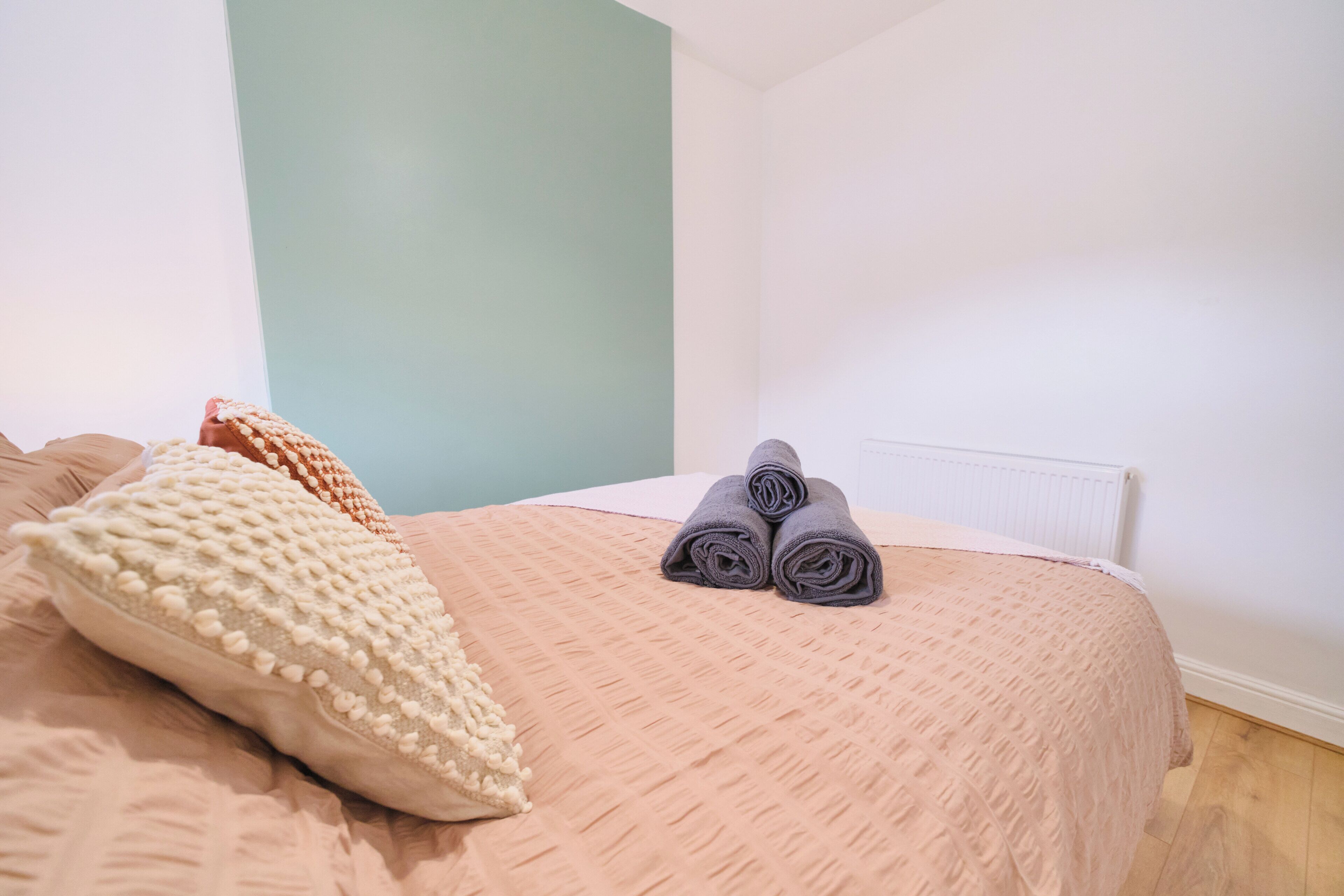 A neatly made bed with a textured bedspread, a rolled-up towel, and a decorative pillow.
