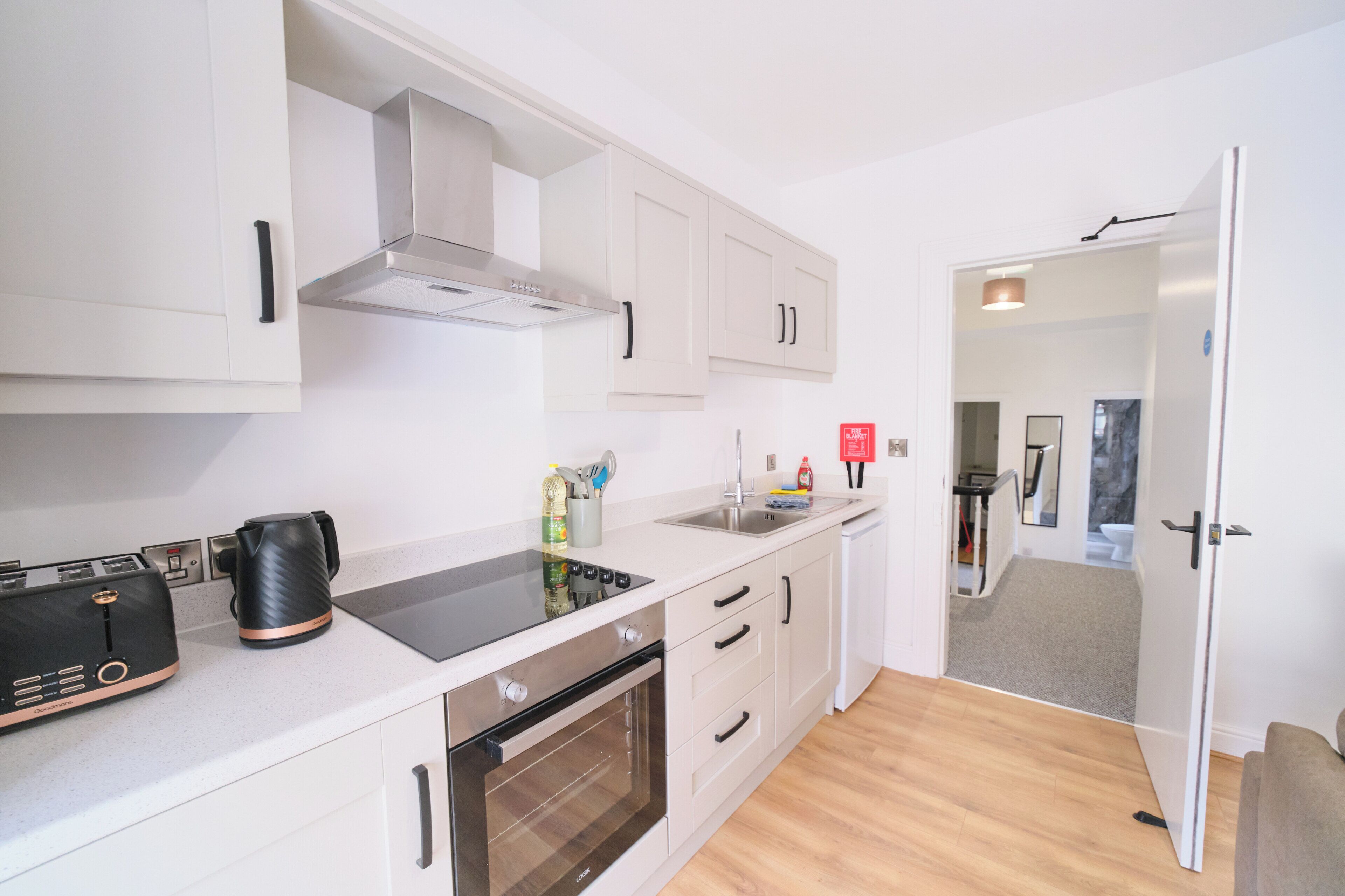 A modern kitchen with white cabinetry, a built-in oven, a kettle, and a sink.
