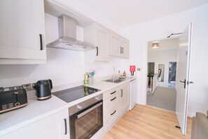 Una cocina moderna con armarios blancos, horno empotrado, hervidor y lavabo.