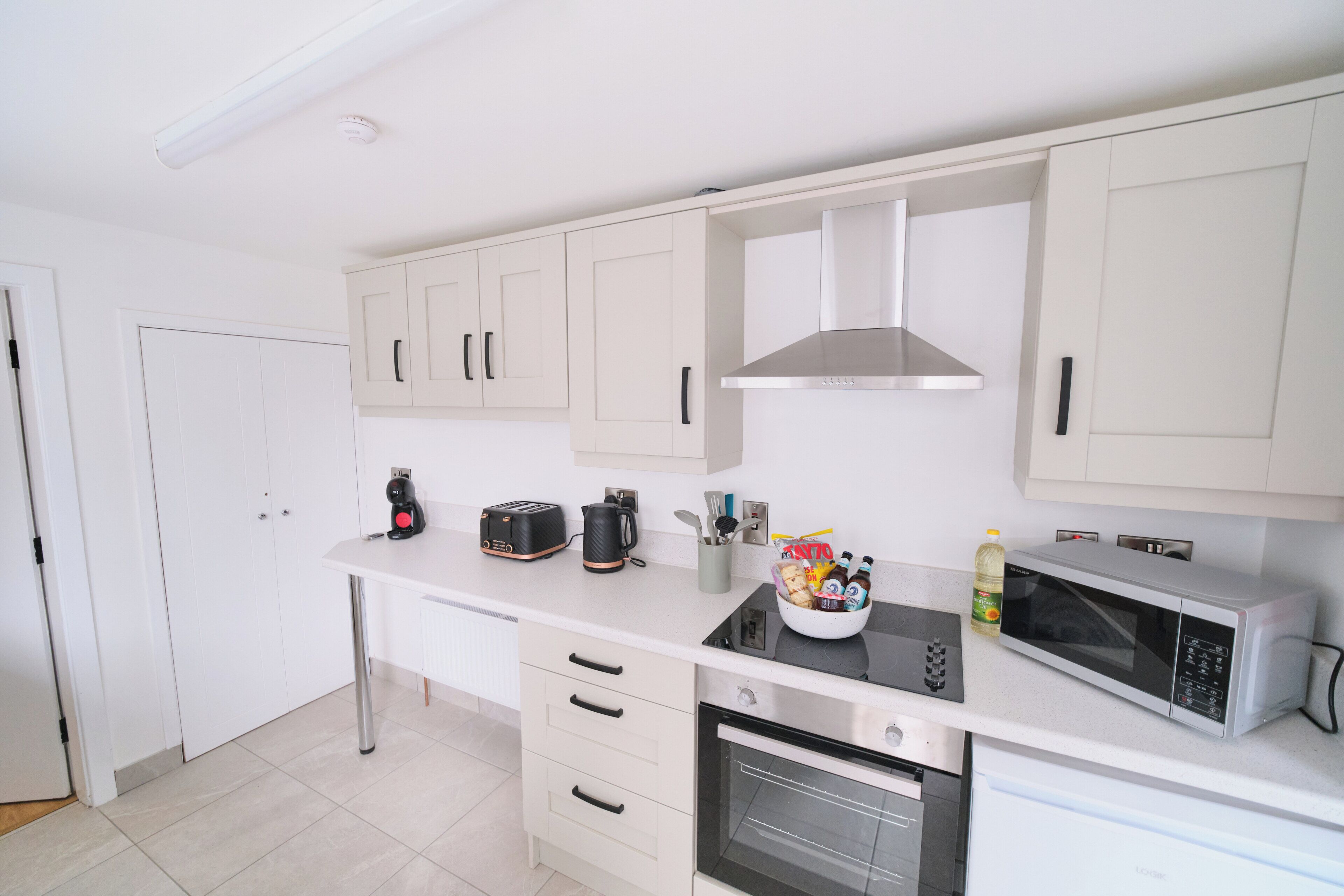 A modern kitchen with white cabinets, a stainless steel range hood, a built-in microwave, and a toaster.