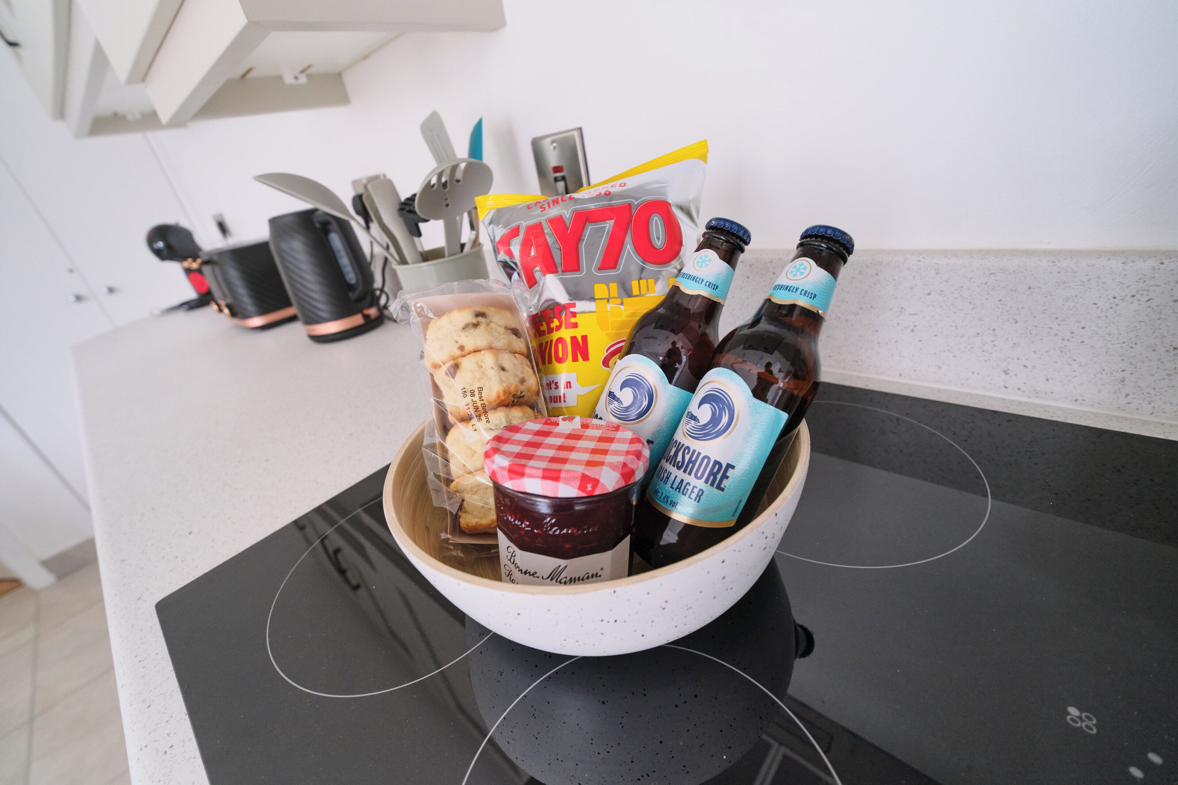 Un comptoir de cuisine avec un bol contenant des biscuits, un pot de confiture et deux bouteilles de bière.
