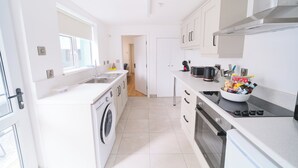 A modern kitchen with a washing machine, oven, and a bowl of snacks on the counter. - Violet and Co (Derry/Londonderry)