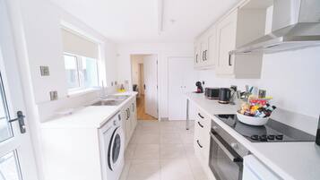 A modern kitchen with a washing machine, oven, and a bowl of snacks on the counter.