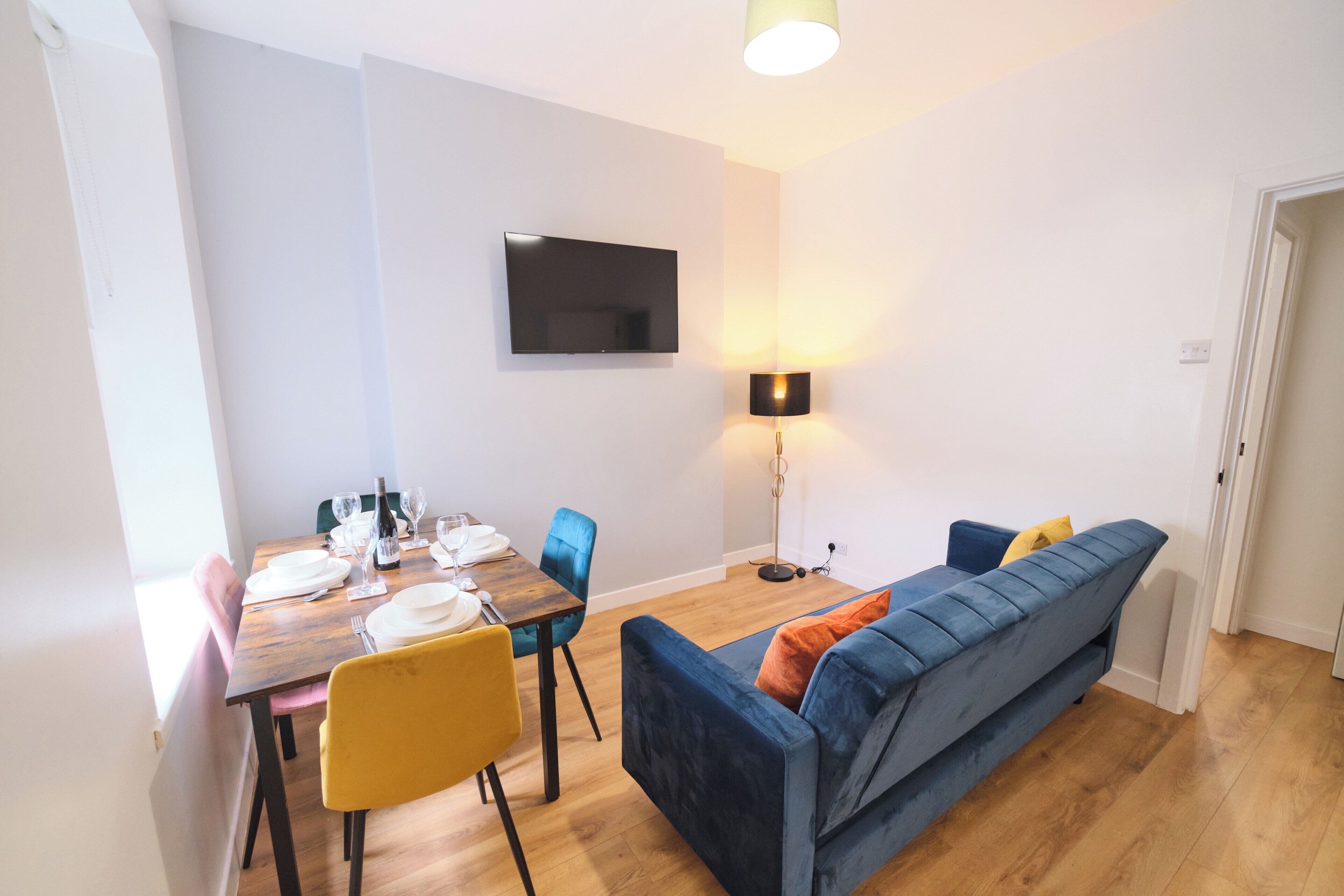 A dining area with a wooden table set for four, a blue sofa, and a floor lamp.