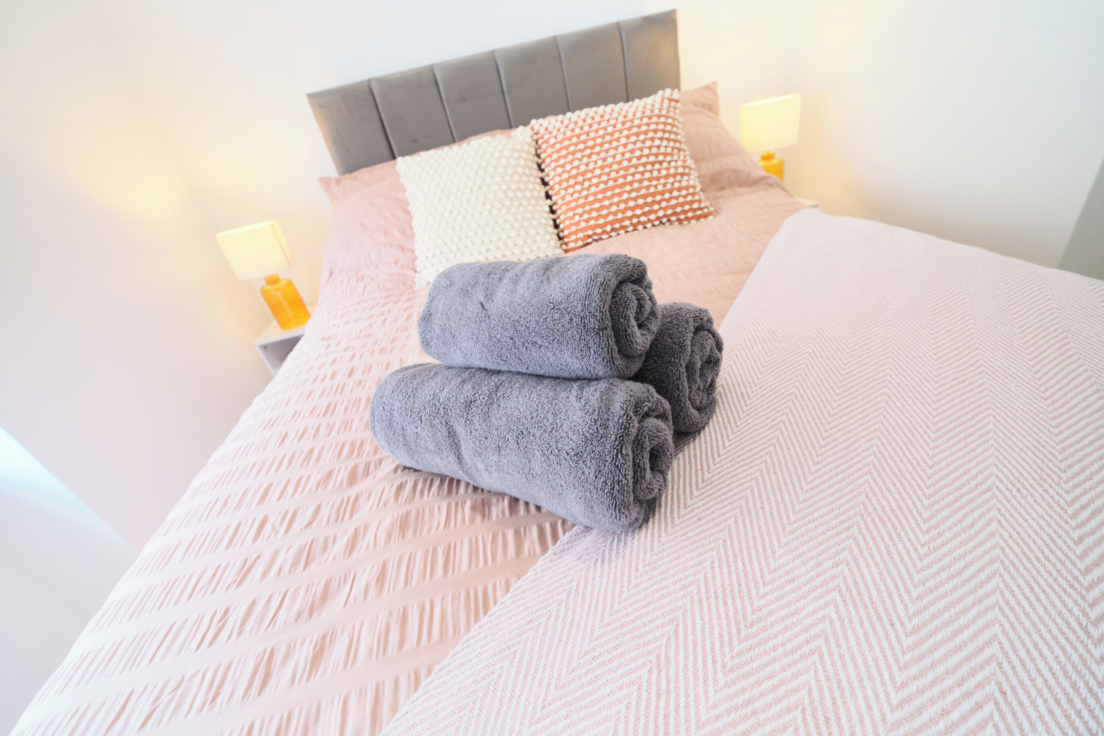 Una cama bien hecha con un edredón estampado, dos toallas enrolladas y una variedad de almohadas.
