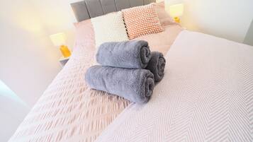 Una cama bien hecha con un edredón estampado, dos toallas enrolladas y una variedad de almohadas.