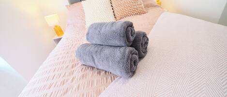 A neatly made bed with a patterned bedspread, two rolled towels, and a variety of pillows.