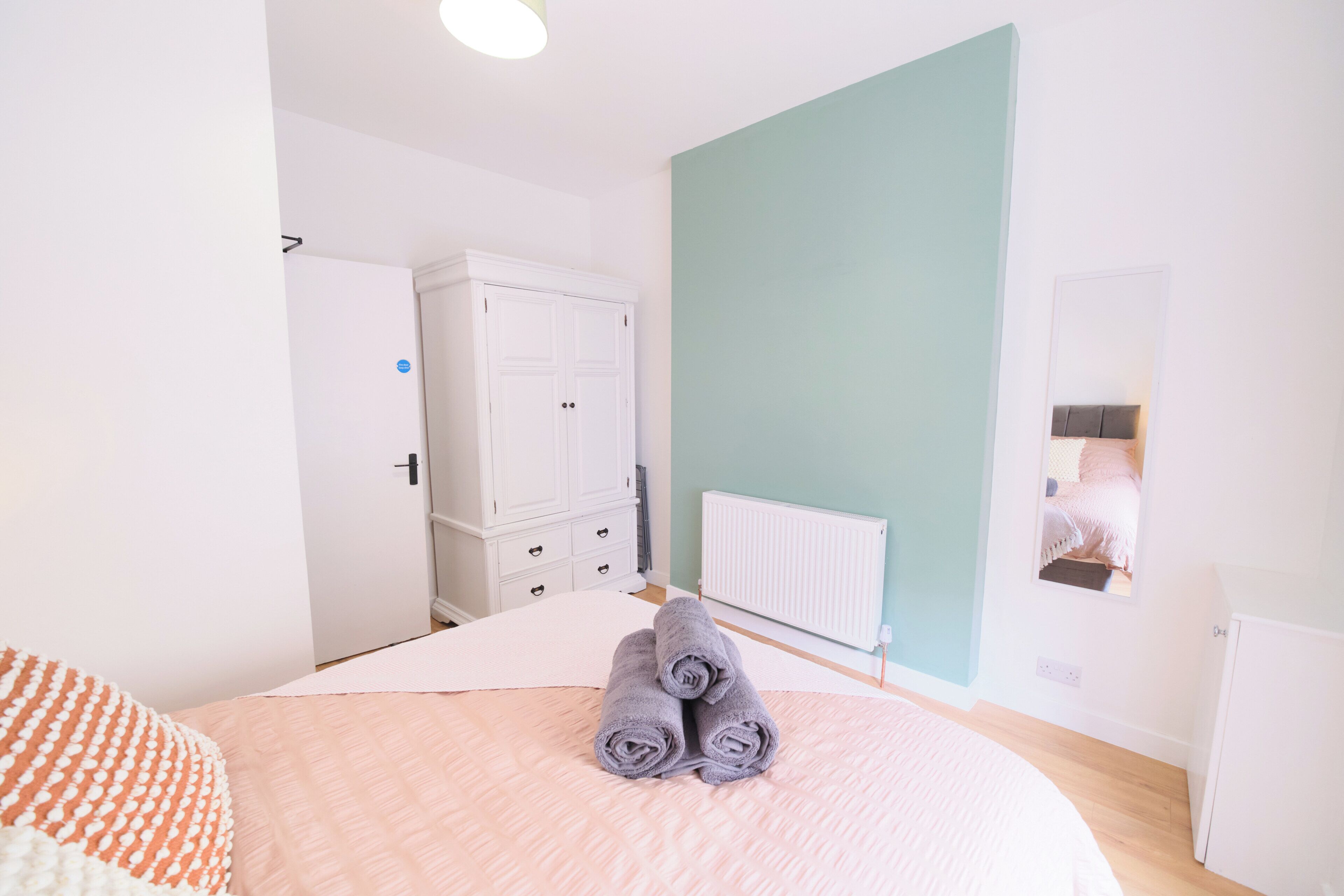 A bedroom with a bed, a wardrobe, a radiator, and a mirror reflecting a bed.
