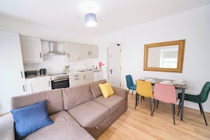 A modern apartment with a kitchenette, a dining area, and a living room with a sofa. - Violet and Co (Derry/Londonderry)
