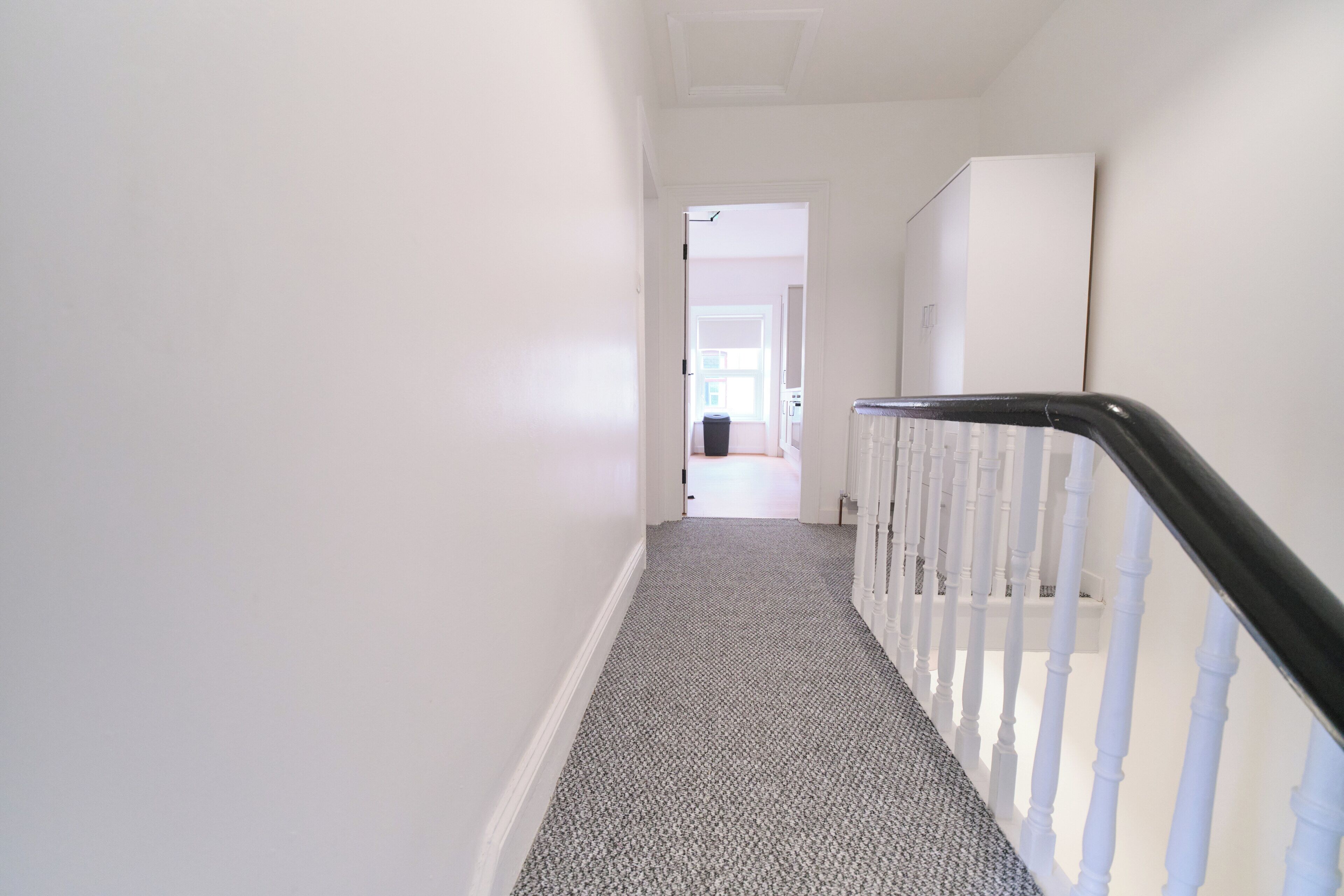 A hallway with a carpeted staircase leading to a room with a window.