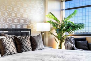 A hotel room with a bed, pillows, a nightstand, a lamp, and a potted plant. - The Rommie 1BR Highrise w/Fast Wi-Fi, Gym (Denver)