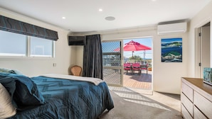 Un dormitorio con cama, televisión, ventana con cortinas, puerta que da a un balcón y un cuadro en la pared.