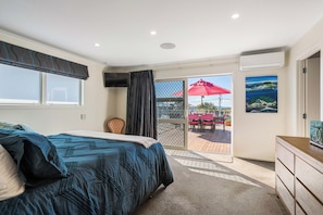 Een slaapkamer met een bed, een televisie, een raam met gordijnen, een deur naar een balkon en een schilderij aan de muur.