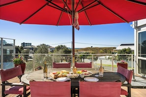 Een houten terras met een rode parasol, een eettafel, stoelen en uitzicht op het landschap.
