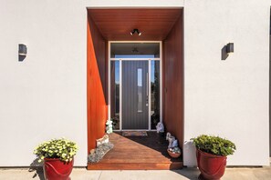 Una entrada moderna amb una rampa de fusta que condueix a una porta de vidre, flanquejada per dos grans testos amb plantes.