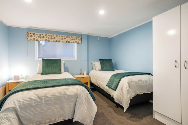 Une chambre avec deux lits, une fenêtre avec un rideau, une armoire et une table de chevet avec une lampe.