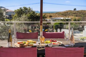 Una taula de dinar plena d'una varietat de plats i vasos de vi, amb un paisatge idíl·lic de fons.