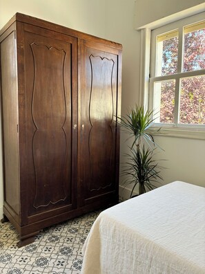 A bedroom with a large wooden wardrobe, a bed with a white bedspread, a potted plant, and a window with a view of trees. - Casa Florentia Apartment. Enjoy the Beaches and Mountains of the Rías Baixas (Sabarís (Baiona))