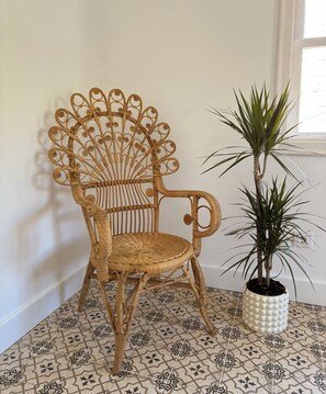 Ein Korbstuhl mit ungewöhnlichem Design, ein Blumentopf und gemusterte Bodenfliesen.