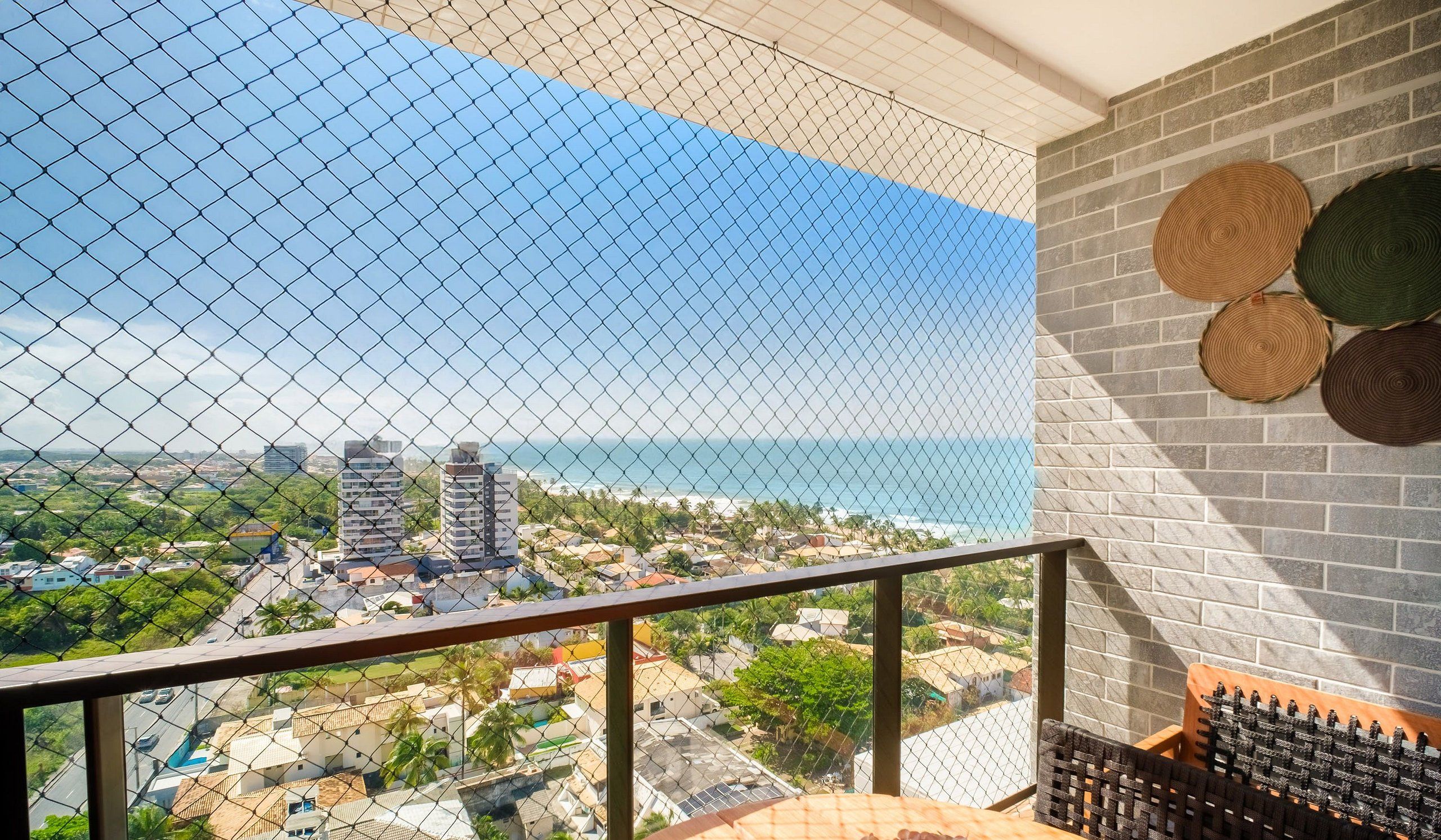 A balcony with a view of the ocean and cityscape, featuring a brick wall and woven coasters.