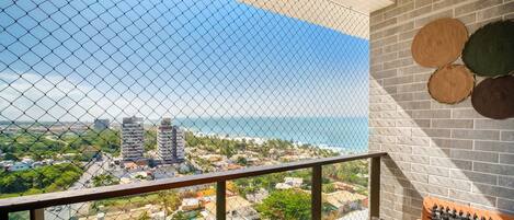 A balcony with a view of the ocean and cityscape, featuring a brick wall and woven coasters.