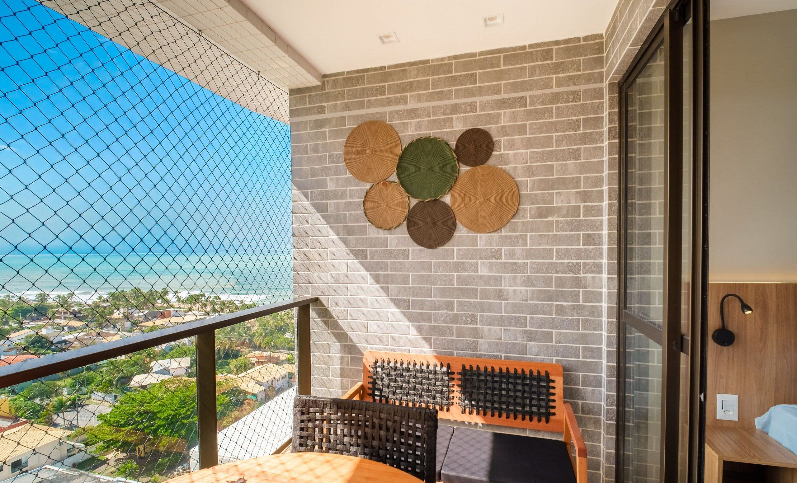 Un balcón con vista al mar, una pared de ladrillo con esteras tejidas y una silla de madera con respaldo de mimbre.