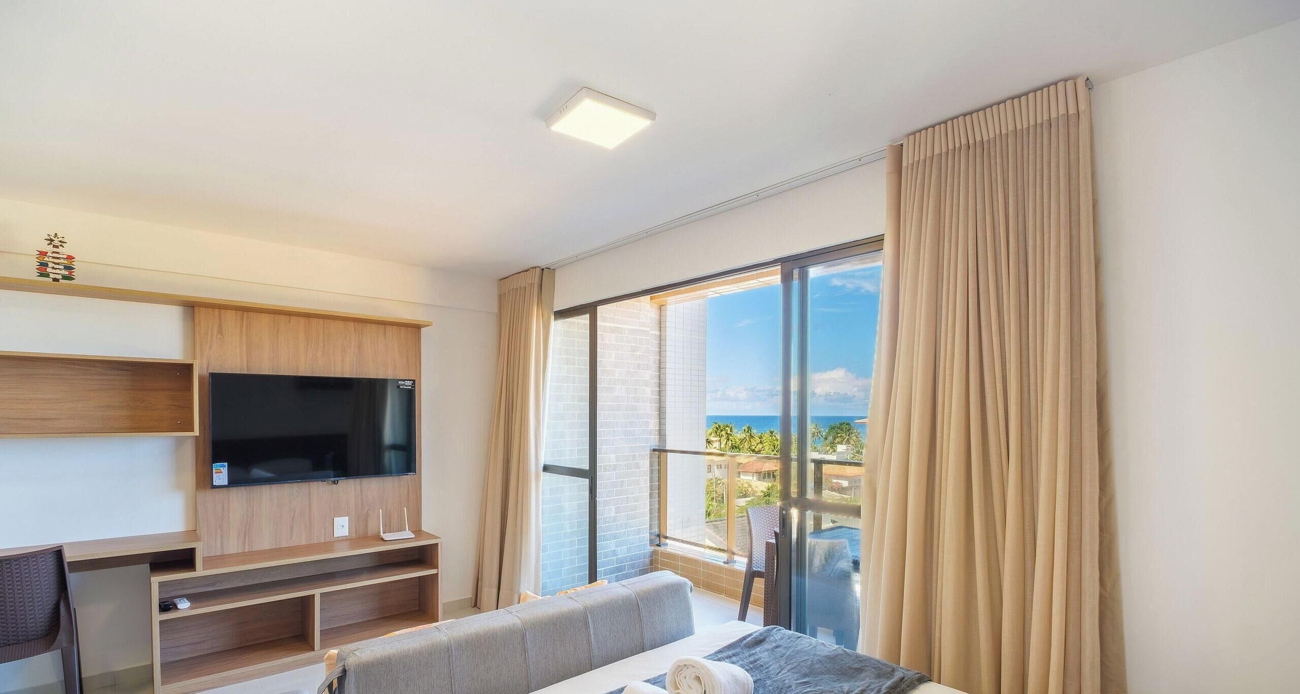 Uma sala de estar moderna com televisão de tela plana, móvel para TV em madeira e uma varanda com vista.