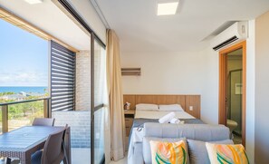 Una habitación de hotel con balcón, una cama con almohadas, un escritorio y vista al mar.