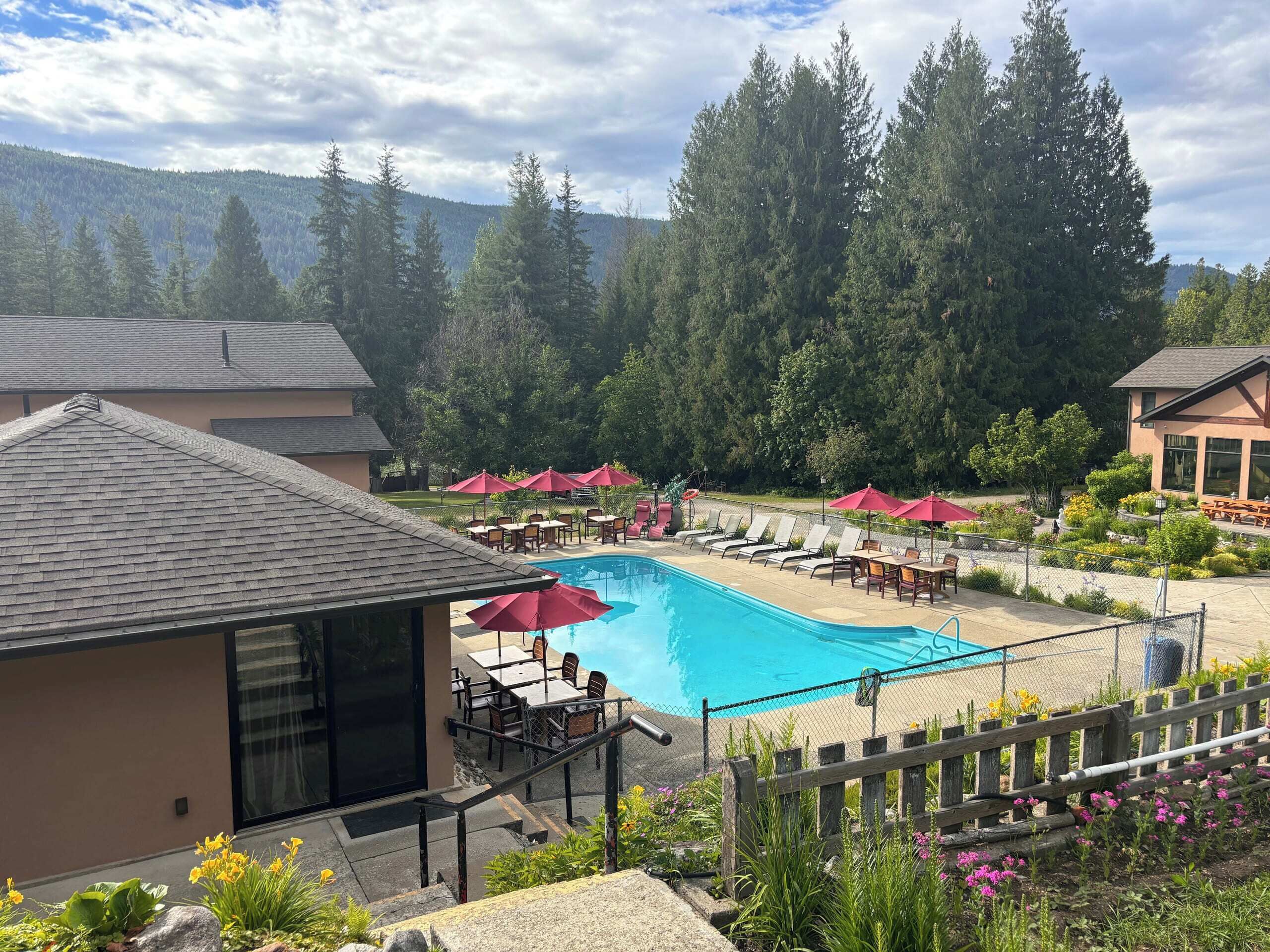 A swimming pool with lounge chairs and umbrellas, surrounded by a fence, with a mountain backdrop.