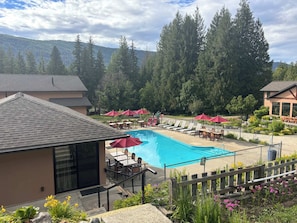A swimming pool with lounge chairs and umbrellas, surrounded by a fence, with a mountain backdrop. - Tahee Mountain Lodge 5 (Mara)