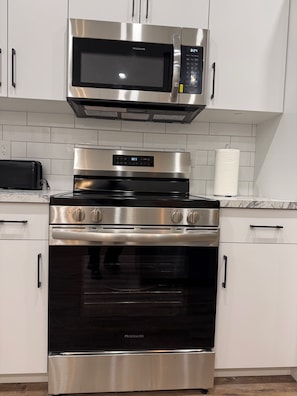 A kitchen with a stainless steel microwave, oven, and a digital clock.