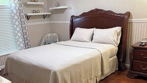 Cama bem arrumada com cabeceira de madeira, mesa de cabeceira com abajur e uma cadeira com almofada.