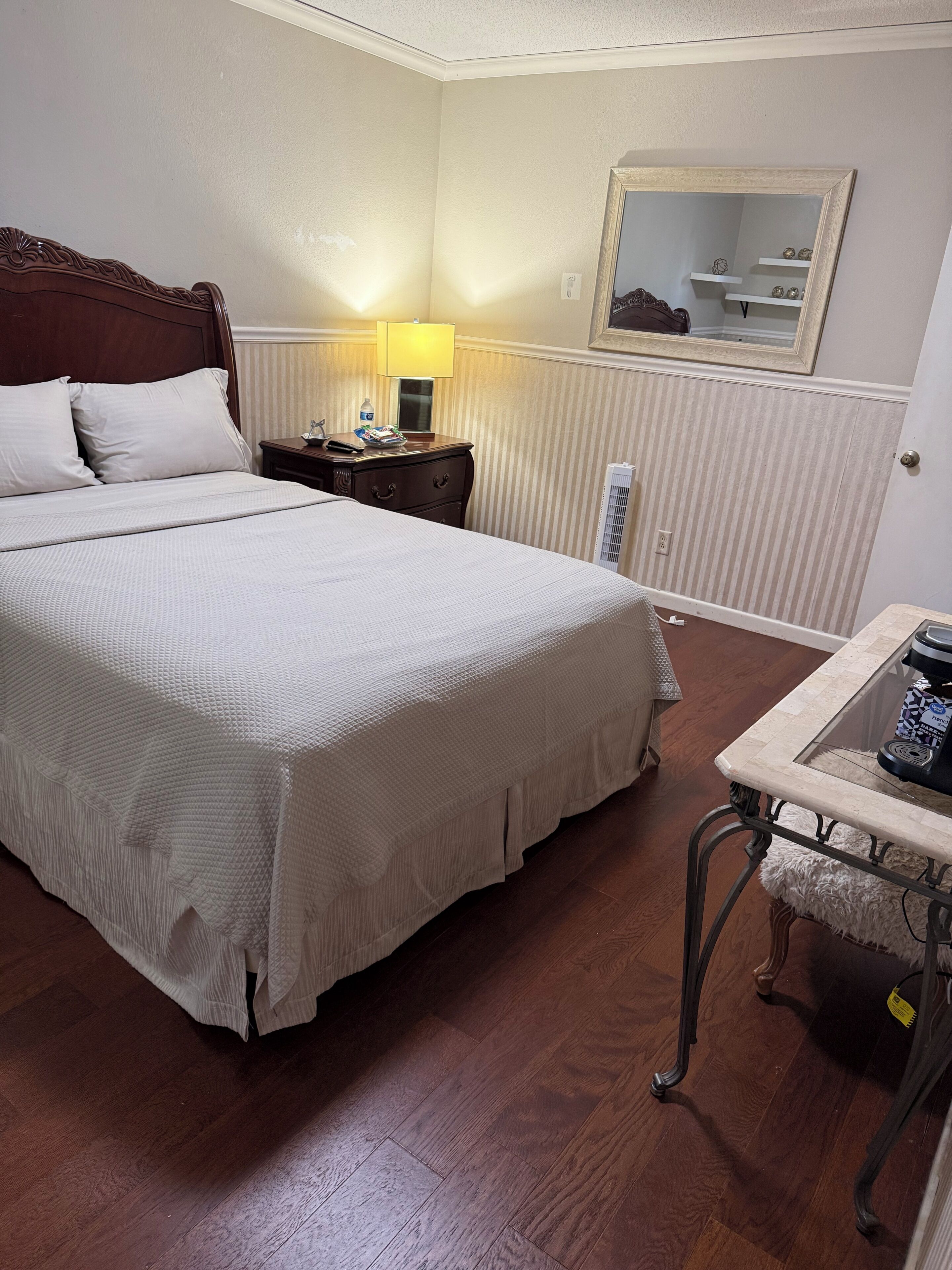 Une chambre d’hôtel avec un grand lit, une table de chevet avec une lampe, une petite table avec une machine à café et un radiateur.