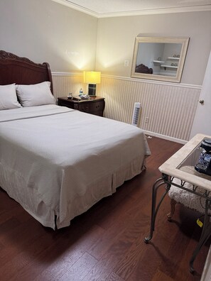 Een hotelkamer met een groot bed, een nachtkastje met een lamp, een klein tafeltje met een koffiezetapparaat en een radiator.