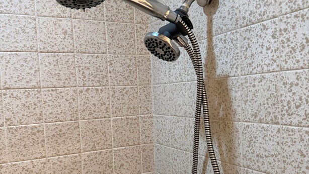 Chuveiro com chuveiro manual e mangueira flexível, instalado em parede revestida com azulejos.