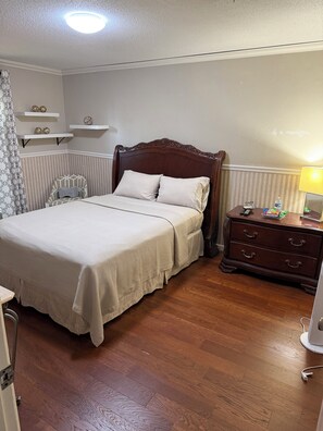 Een keurig opgemaakt slaapkamer met een houten bed, nachtkastjes en een stoel.