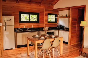 A wooden interior with a kitchen and dining area, including a refrigerator, stove, and table set for two.