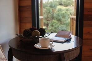 Una mesa redonda con una taza y platillo blancos, un libro y un piñón como centro de mesa.