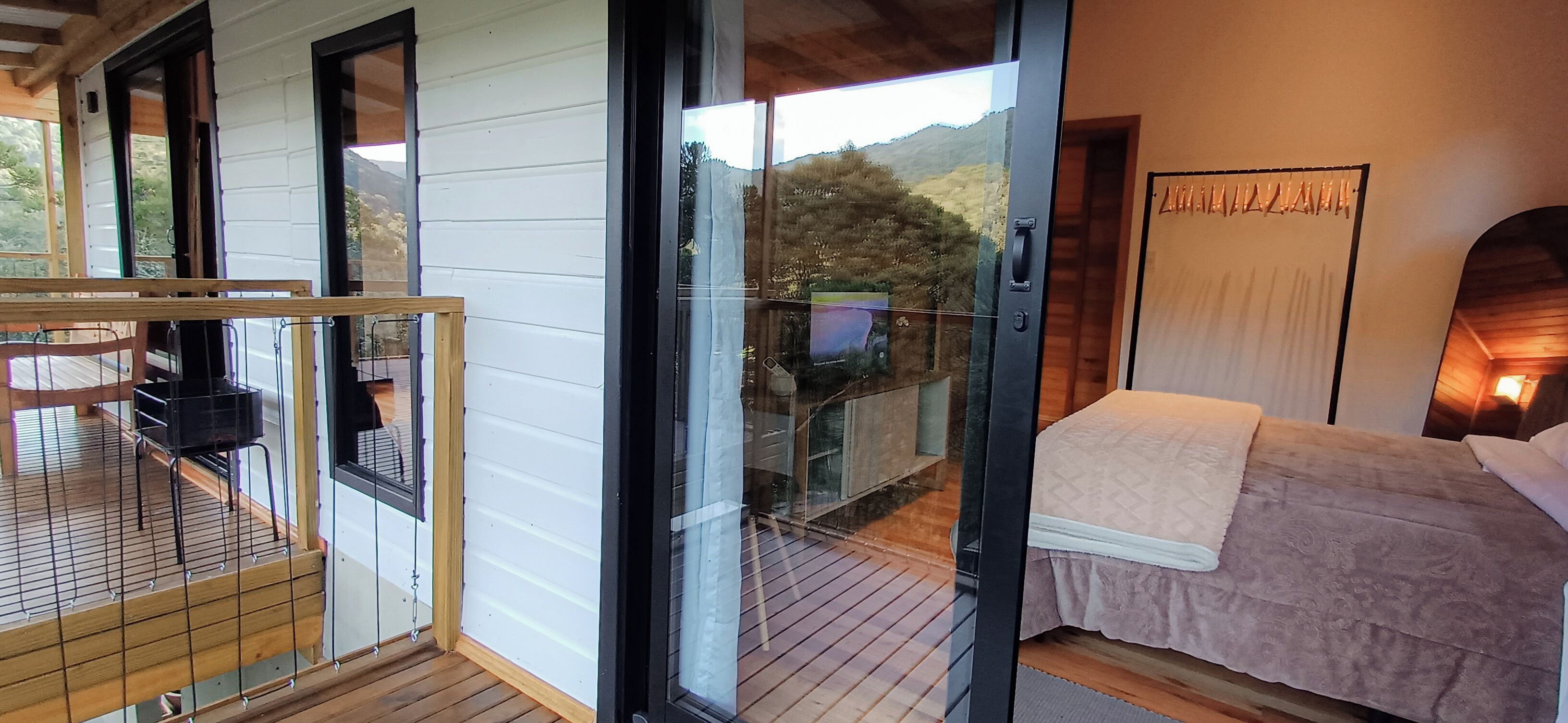 A bedroom with a bed, a wooden floor, a glass door leading outside, and a view of the outdoors.