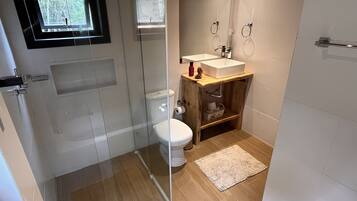 A modern bathroom with a glass shower enclosure, a white toilet, a wooden vanity with a sink, and a small rug on the floor.