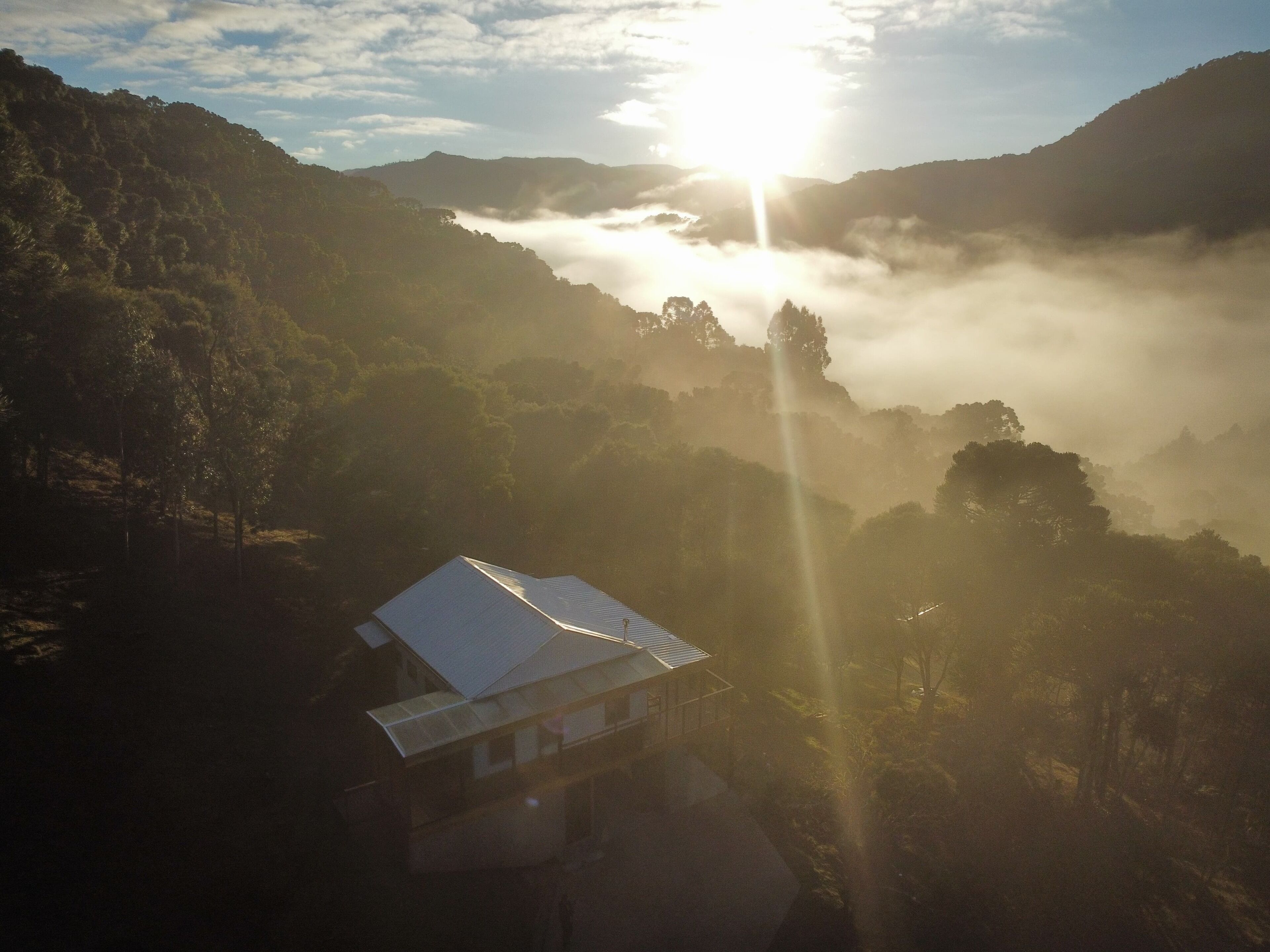 A building with a flat roof, surrounded by forested hills and a sunrise.