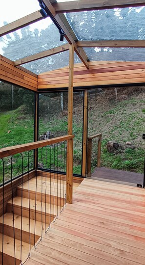 A wooden deck with a glass enclosure, metal railing, and a view of a green landscape.