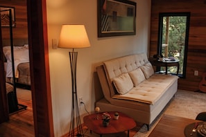 Una habitación acogedora con sofá, lámpara de pie, una mesita con un florero y ventana con vistas al verdor.