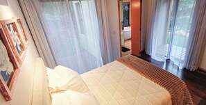 A bedroom with a bed, a window with curtains, and a door leading to a bathroom.