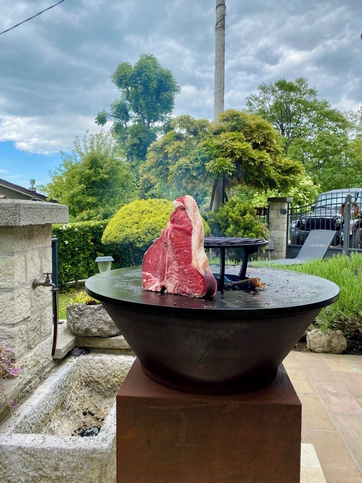 A large outdoor stone basin with a piece of meat on top, surrounded by greenery and a stone structure.