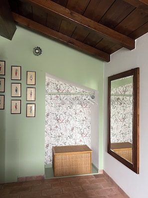 Ein Zimmer mit Holzboden, einem an der Wand befestigten Spiegel, einem Korbwägelchen und einem Vorhang mit Blumenmuster.