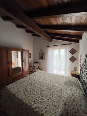 A bedroom with a large bed, wooden wardrobe, and a chair.